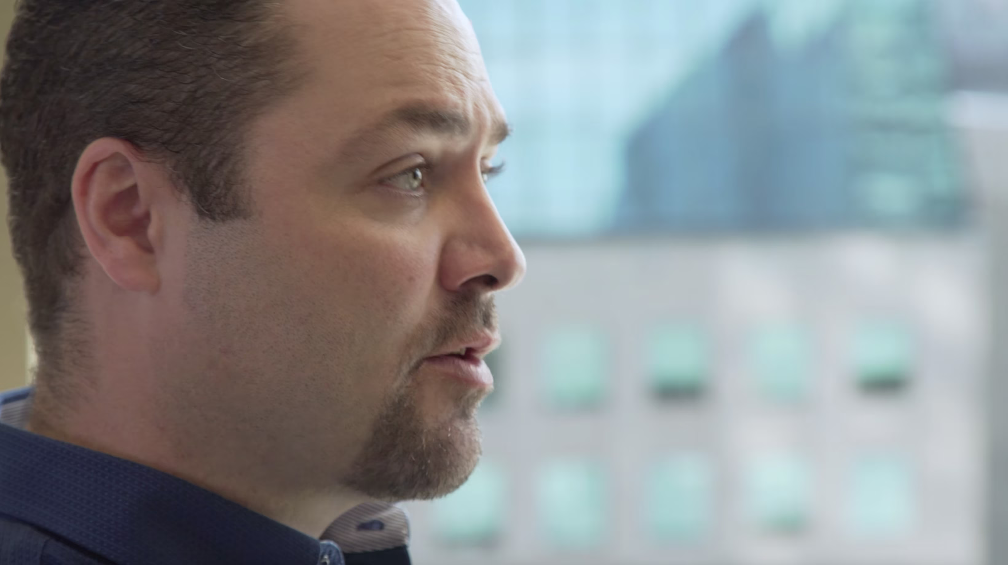 Profile view of a man speaking during a workplace conversation in an office setting.