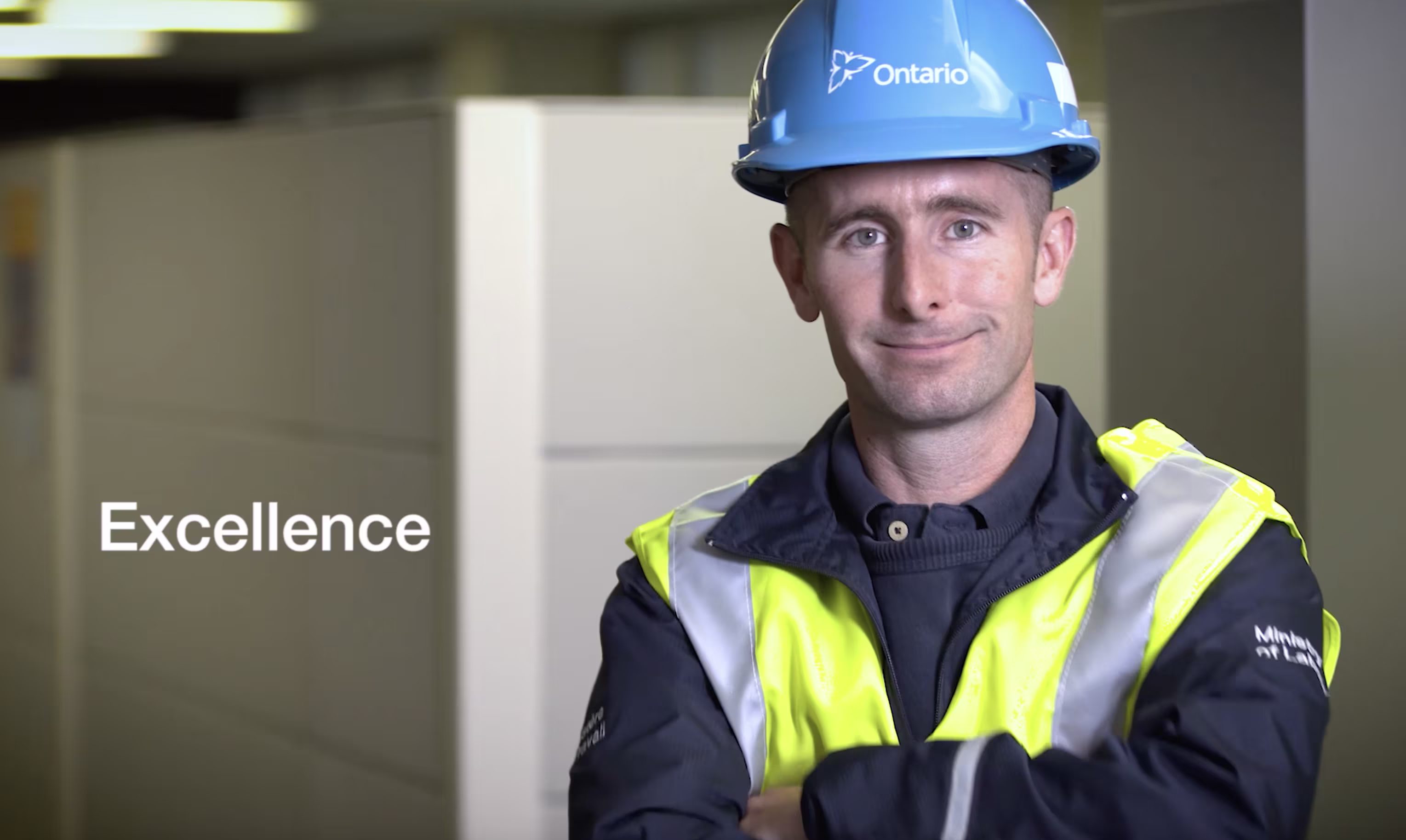 Construction worker wearing a blue Ontario hard hat and high-visibility safety vest standing with arms crossed, representing workplace excellence.