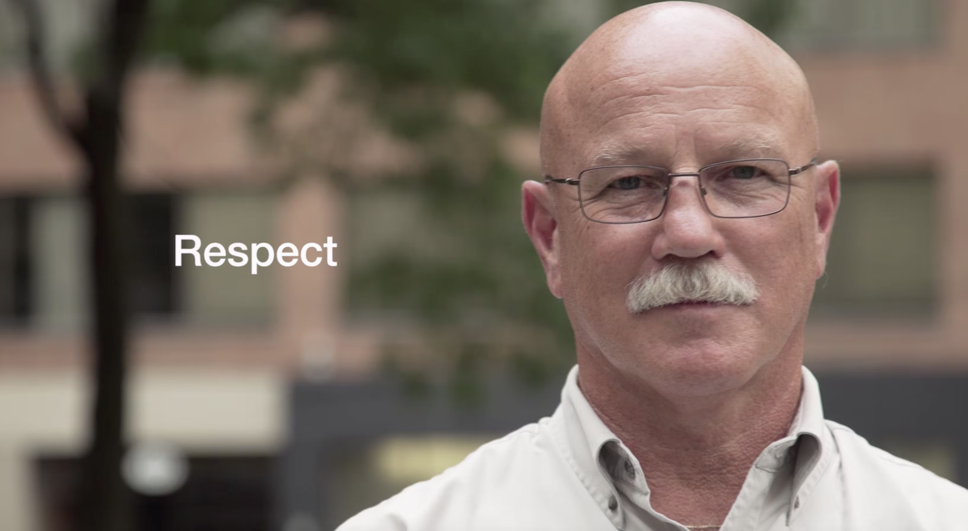 Portrait of an older man with glasses and a mustache outdoors, representing respect and leadership in the workplace.